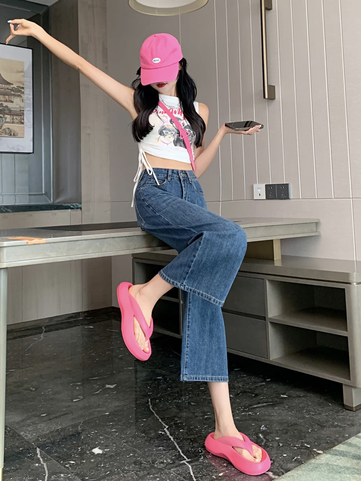 YEEYEEWang 빈티지 블루 와이드레그 진, 아시안핏, 테이블에 앉은 전신 측면 포즈로 한 팔을 올리고 다리를 들어 올리며 폰을 들고, 핑크 캡.