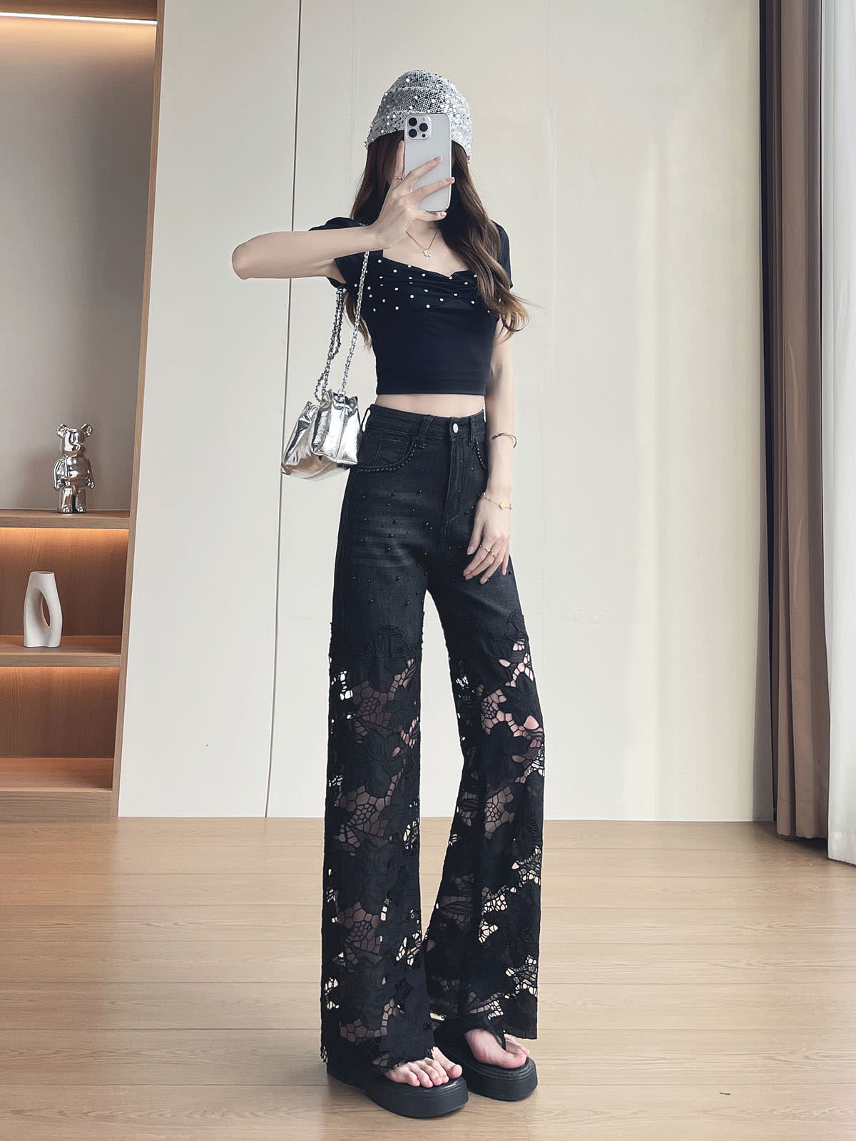 YEEYEEWang 솔리드 블랙 와이드레그 진, 아시안핏, 전신 정면 포즈로 휴대폰을 얼굴 앞에 들고 다른 손은 허벅지에, 스팽글 버킷햇과 실버 백.