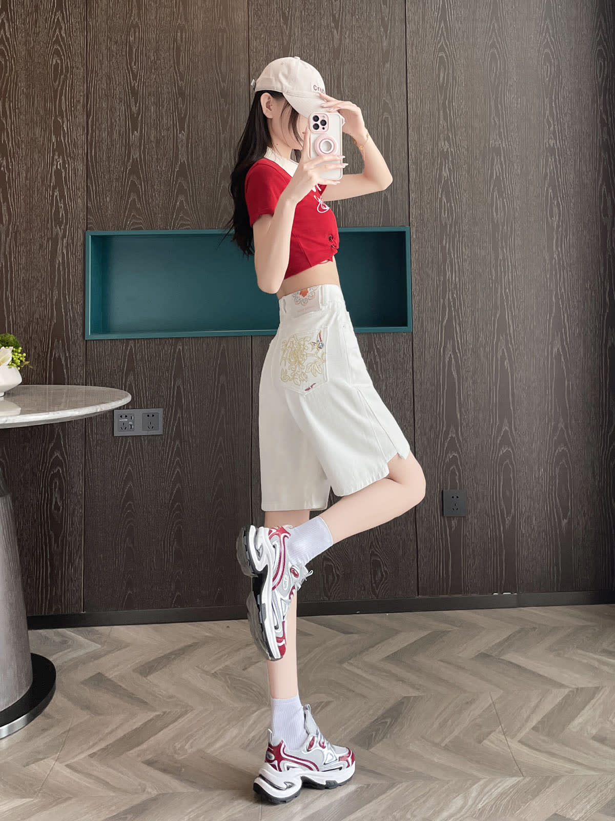 YEEYEEWang 화이트 데님 버뮤다 쇼츠, 아시안핏, 전신 측면 뷰, 한쪽 다리 뒤로 들어 올린 포즈, 얼굴 앞 폰, 뒷주머니 자수 포인트.
